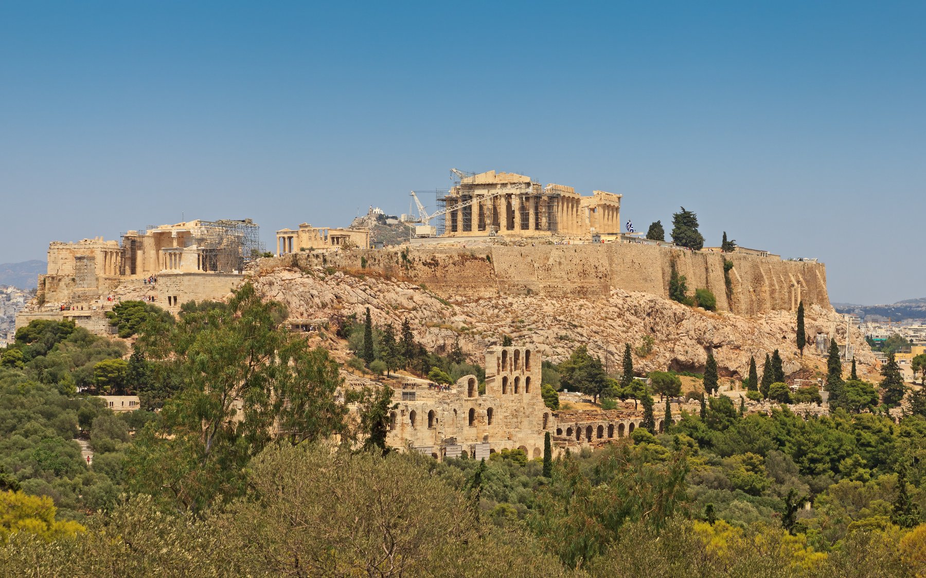 View of the Acropolis of Athens from Philopappos Hill at sunset, the Parthenon and Erechtheion silhouetted on the limestone summit above the city.