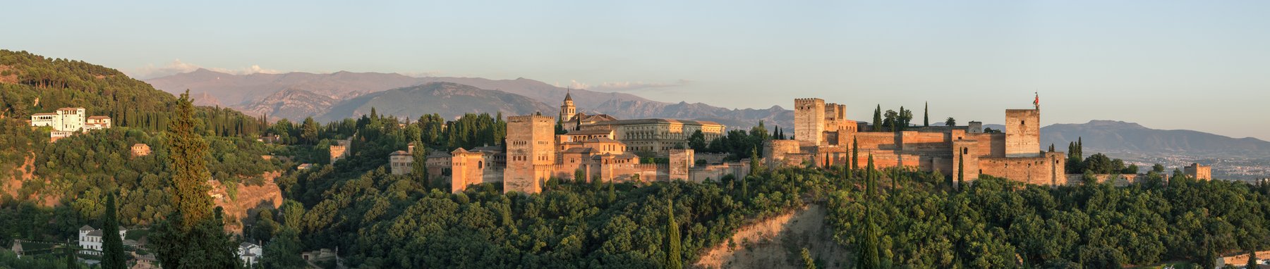 Evening view of the Alhambra palace complex in Granada from the Mirador San Nicolás, the red walls of the citadel and the Nasrid Palaces above the city with the Sierra Nevada mountains rising behind.