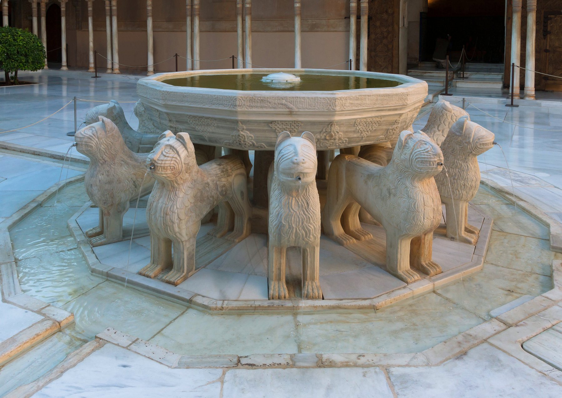 The Court of the Lions in the Nasrid Palaces of the Alhambra, with the central fountain held up by twelve marble lions and the surrounding arcade of slender columns supporting carved stucco arches.