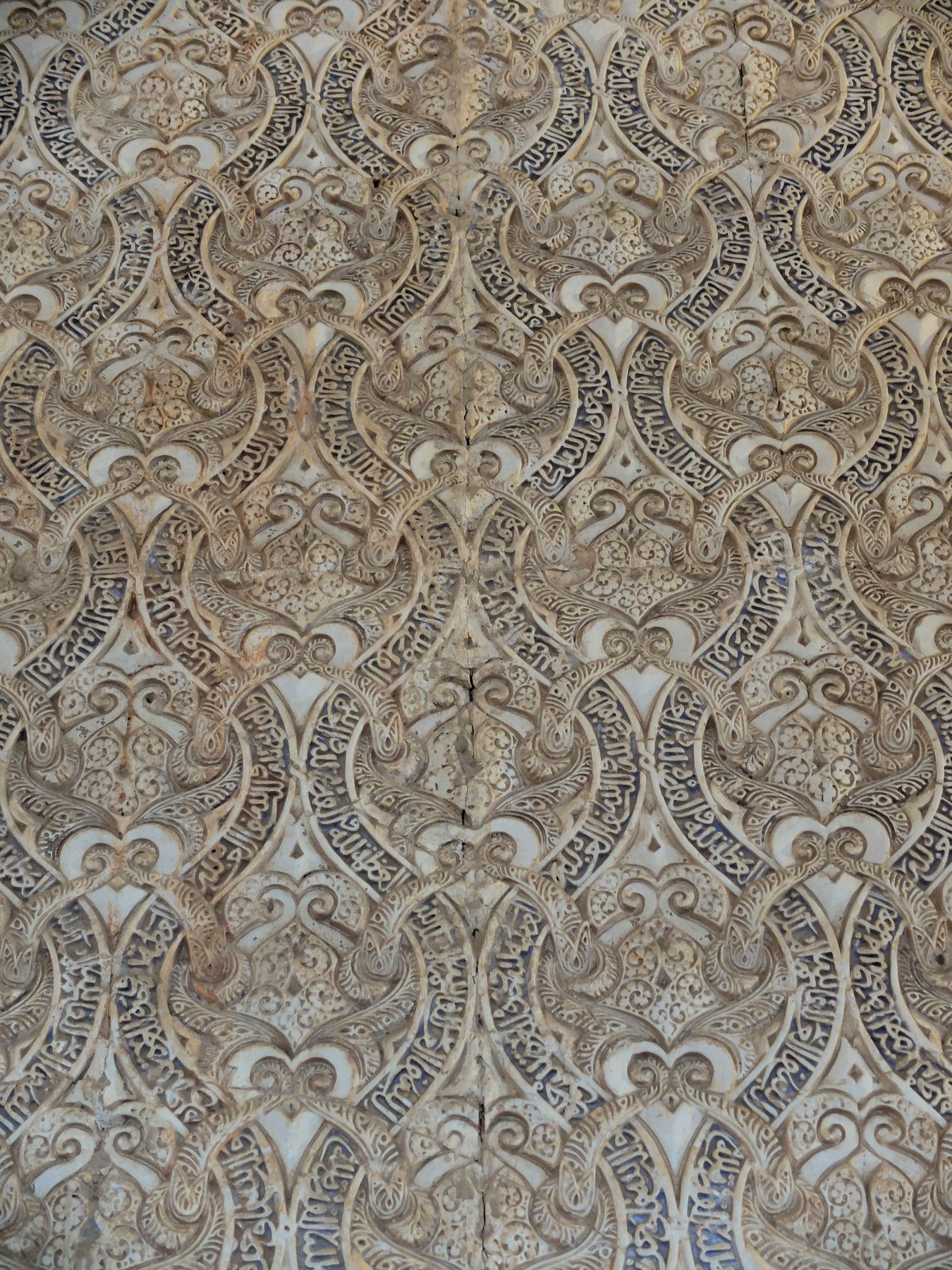 The interior of the Comares Hall in the Alhambra, with carved stucco and tile mosaics covering the walls in dense geometric and calligraphic patterns rising to a wooden coffered ceiling.