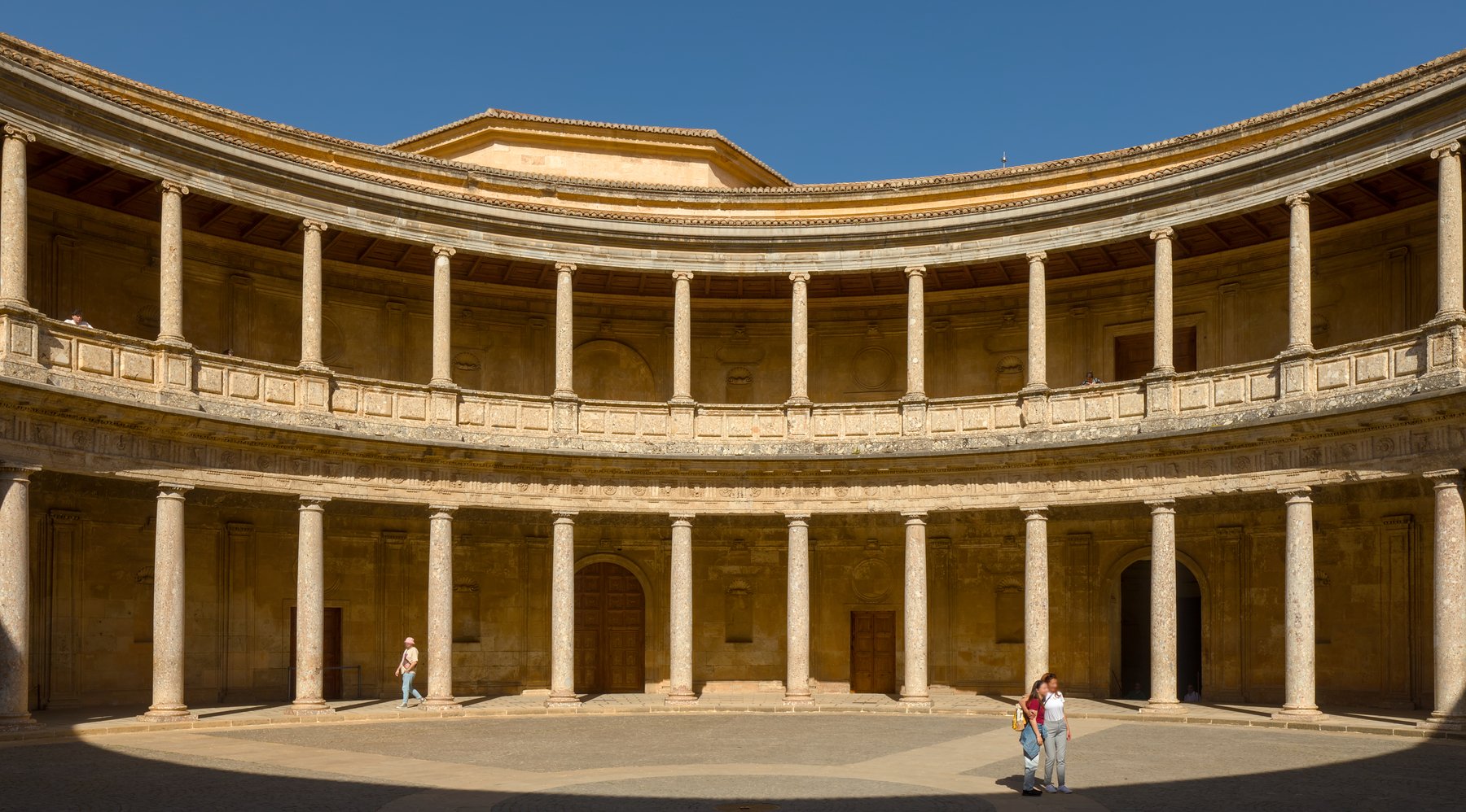 The Renaissance Palace of Charles V in the Alhambra, a square Italianate building of dressed stone with a circular two-story arcaded courtyard at its center, set among the older Moorish walls of the citadel.