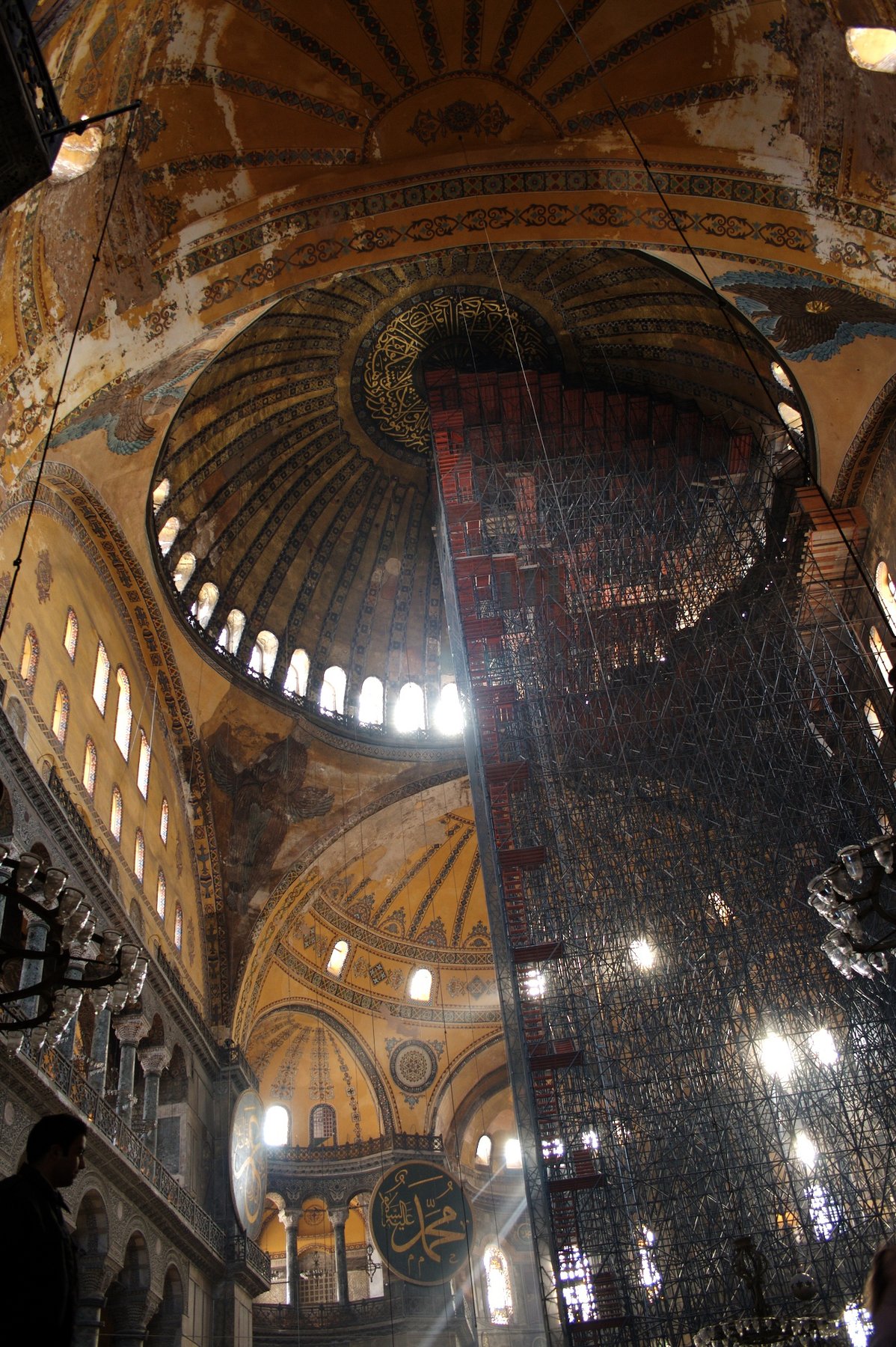 Looking up into the central dome of Hagia Sophia from the nave, with Islamic calligraphic medallions on the pendentives and a ring of windows at the base of the dome.