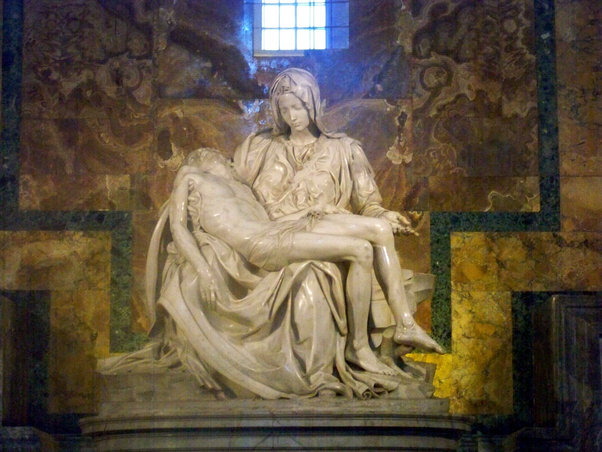 Michelangelo's Pietà in its chapel at St. Peter's Basilica, the Virgin holding the body of Christ across her lap.