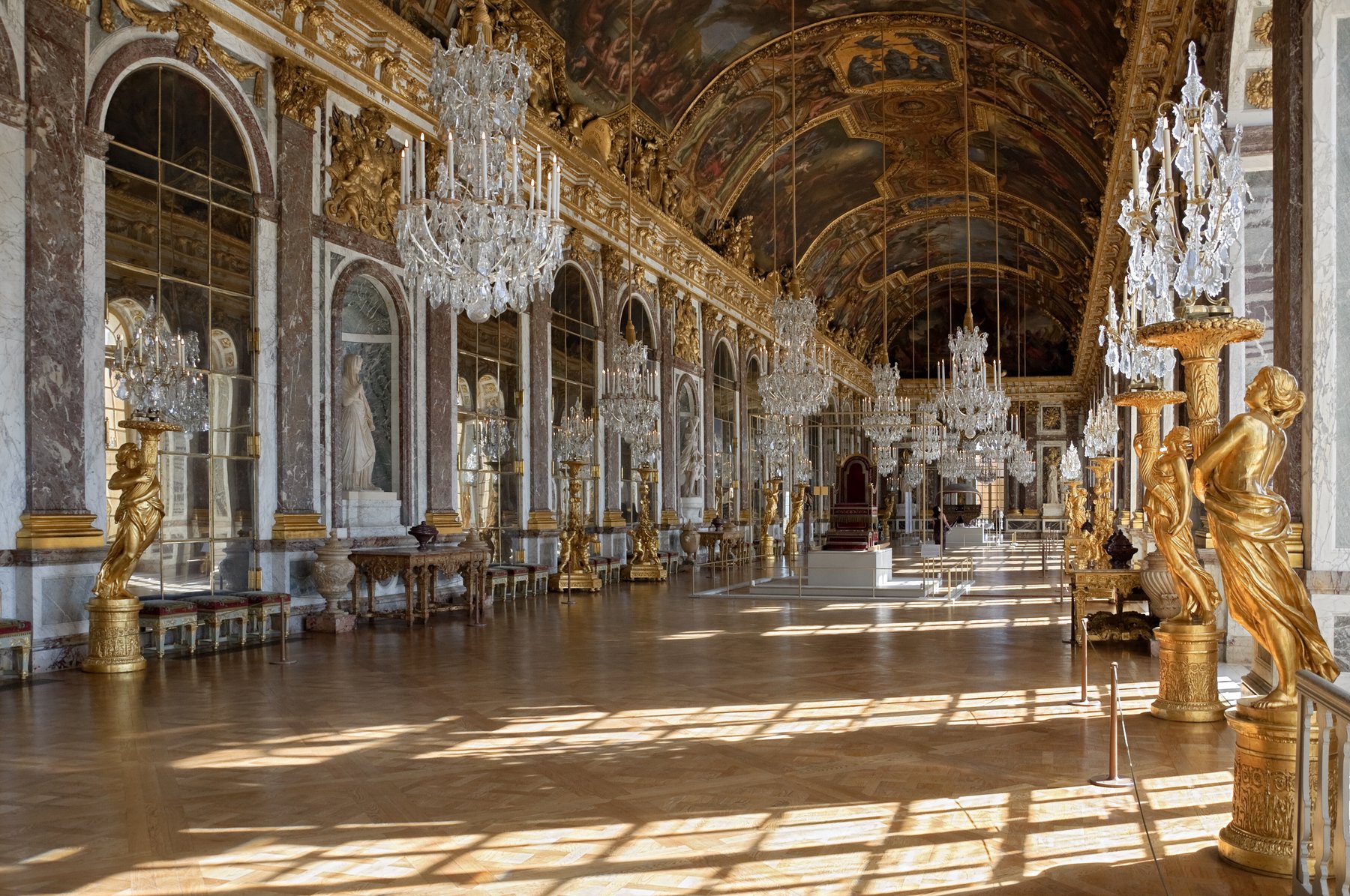 The Hall of Mirrors in the Palace of Versailles, a seventy-three-meter-long gallery lined with seventeen arched mirrors facing seventeen tall windows that open onto the gardens, with crystal chandeliers and a frescoed barrel-vaulted ceiling above.