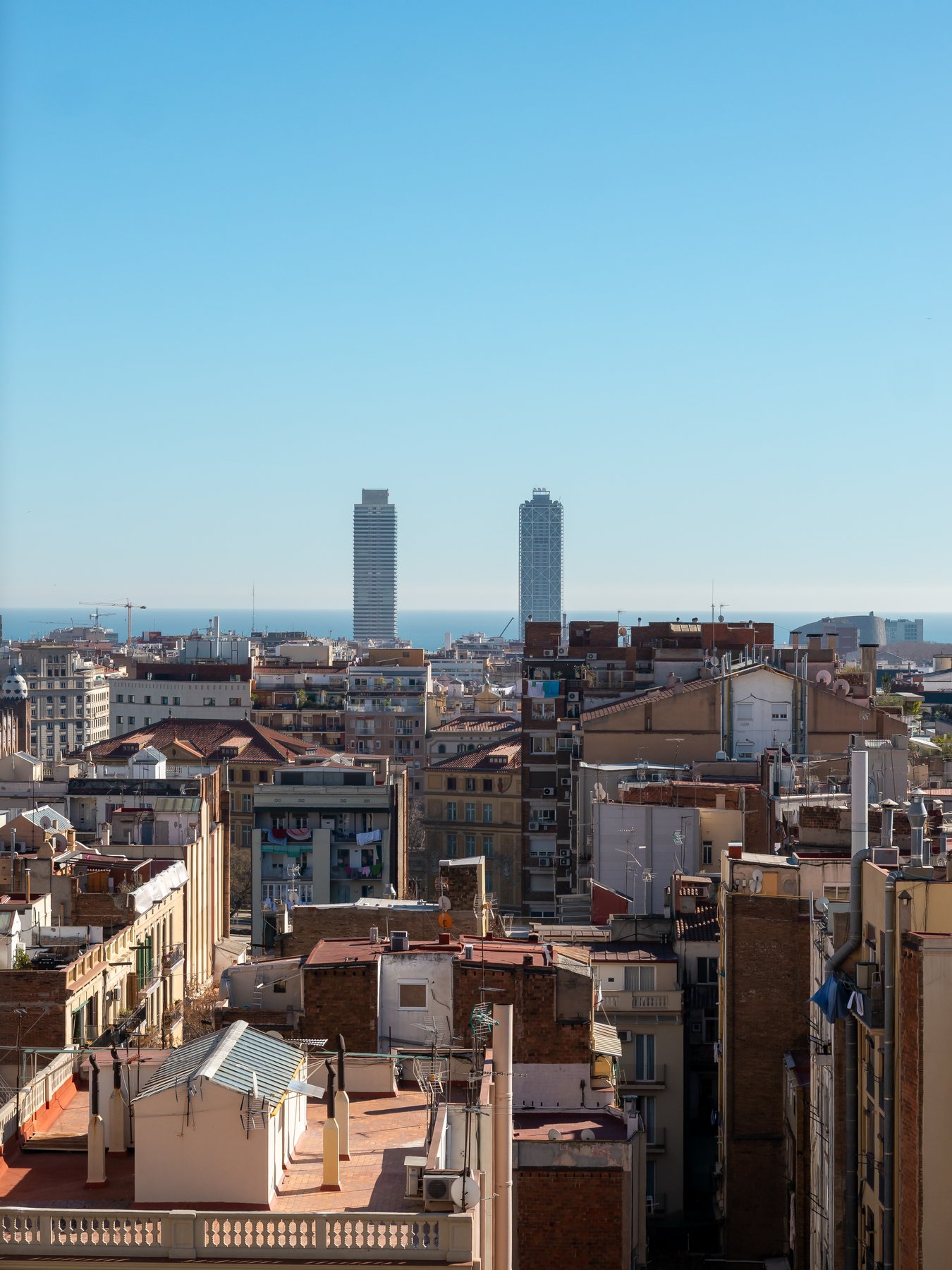 The exterior of the Sagrada Familia basilica in Barcelona, with the four spires of the Passion facade rising on the left and the older stone of the Nativity facade visible on the right, scaffolding wrapping the central tower in progress.