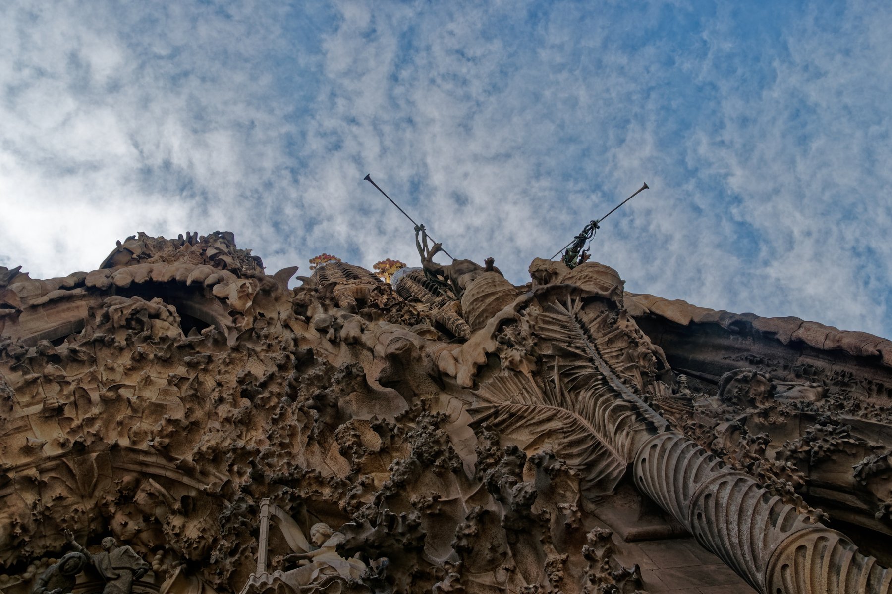 A close view of the Nativity facade of the Sagrada Familia, encrusted with stone figures, animals, plants, and angels carved in dense relief around the central tympanum showing the birth of Christ.
