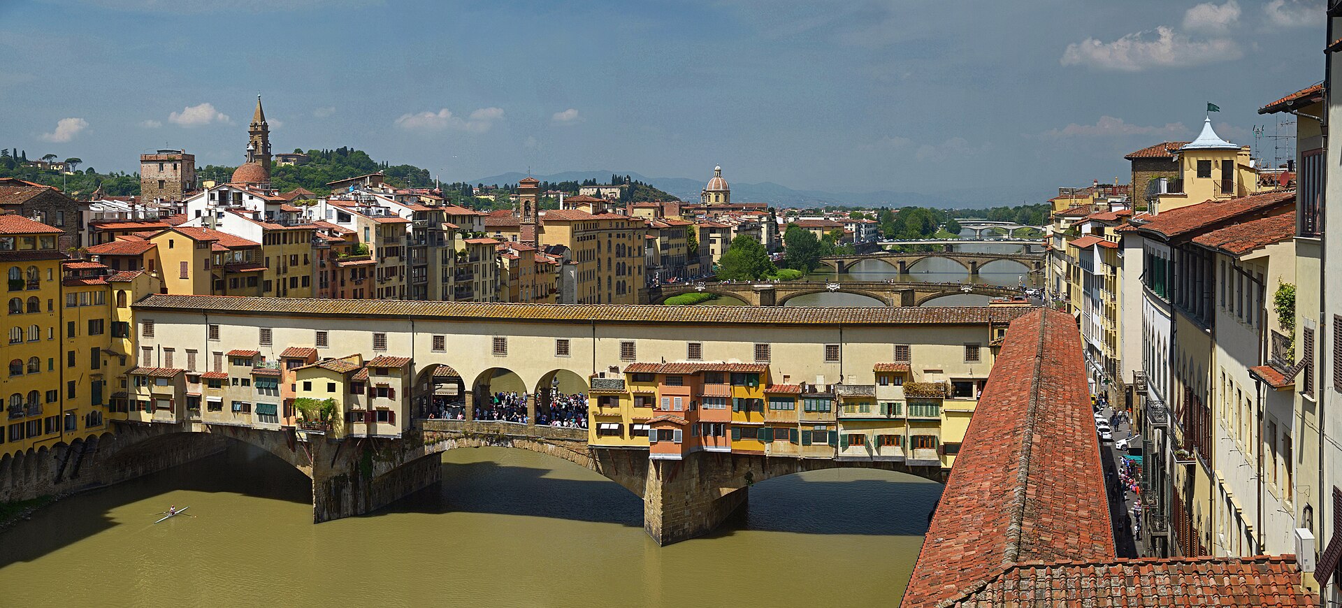 View from the South Corridor windows, looking west along the Arno toward the Ponte Vecchio. The Vasari Corridor — the covered passage Cosimo I built so the Medici could walk between Palazzo Vecchio and the Pitti Palace without entering the street — runs over the top of the bridge.